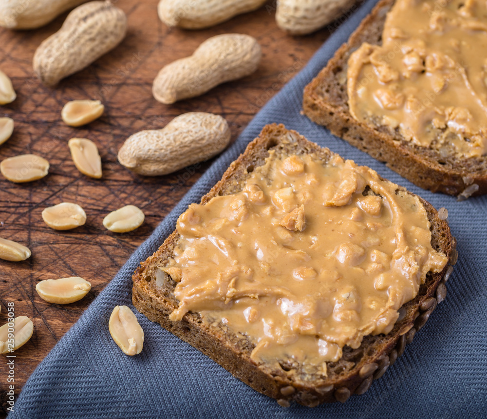 Fototapeta premium Bread spread with peanut butter on grey napkin.