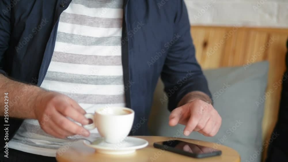 Happy Caucasian Businessman in Formal Clothes Smiling and Looking at His Smartphone Screen While Drinking Coffee In Indoors Cafe During Lunch Time. Happy Caucasian Businessman in Formal Clothes Smiling and Looking at His Smartphone Screen While Drinking Coffee In Indoors Cafe During Lunch Time.