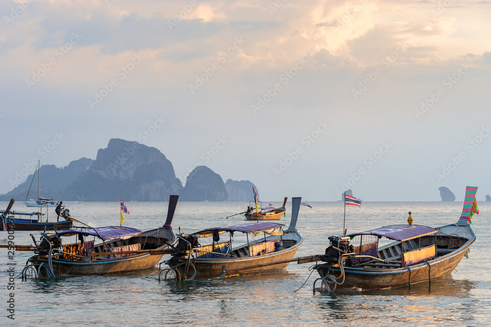 Several moored thai traditional long-tail boat in the sea water near the shore at sunset