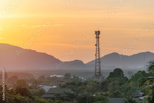 High telecommunication cell tower antenna in asian countryside nature on the background of the silhouettes of the mountains at beautiful orange sunset