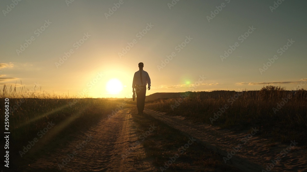 businessman in sunglasses goes down the country road with a briefcase in his hand. The entrepreneur works in a rural area. a farmer inspects land at sunset. agricultural business concept.