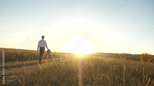 businessman in sunglasses goes down country road with briefcase in his hand. agricultural business concept. The entrepreneur works in a rural area. farmer inspects the land at sunset. Slow motion © zoteva87