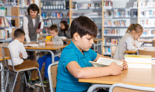 Tween boy reading textbooks in school library