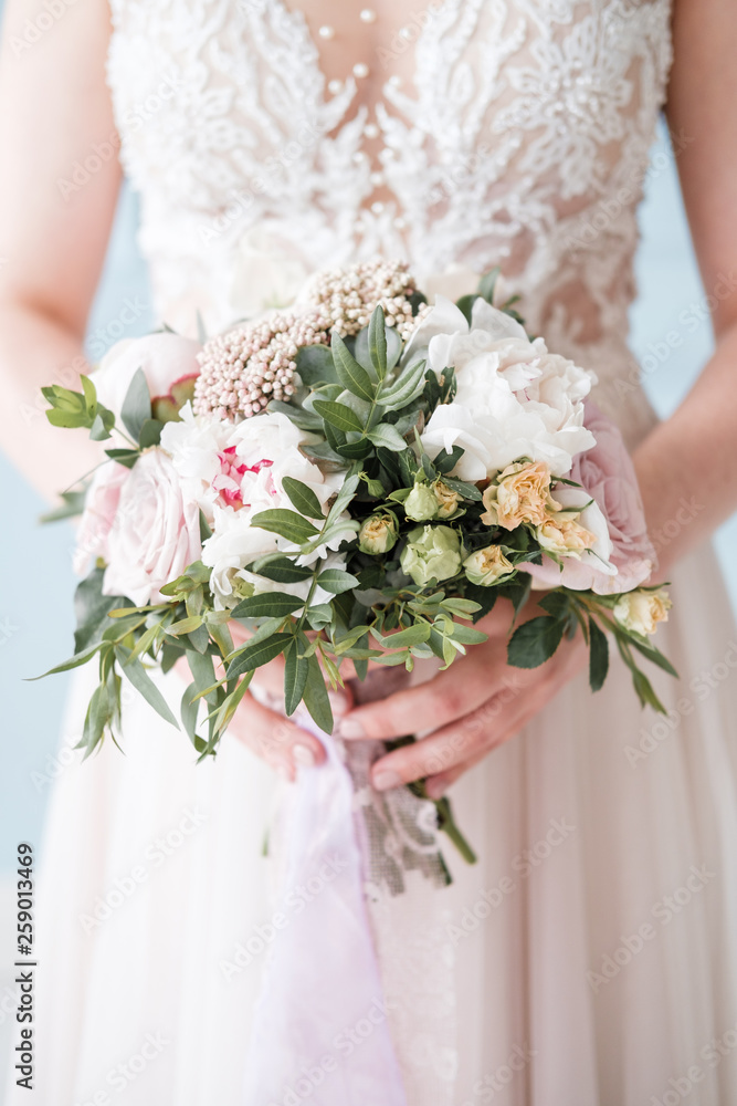 Bridal bouquet with pink and cream roses in the hands of the bride.