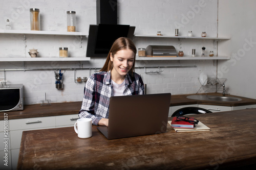 Young woman working at home in the morning. Girl drinking coffee. She is using her laptop