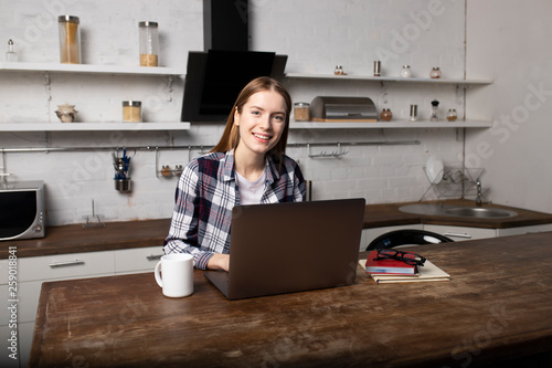 Young woman working at home in the morning. Girl drinking coffee. She is using her laptop