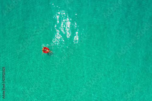 Aerial view of slim woman swimming on the swim ring donut in the transparent turquoise sea in Seychelles. Summer seascape with girl, beautiful waves, colorful water. Top view from drone