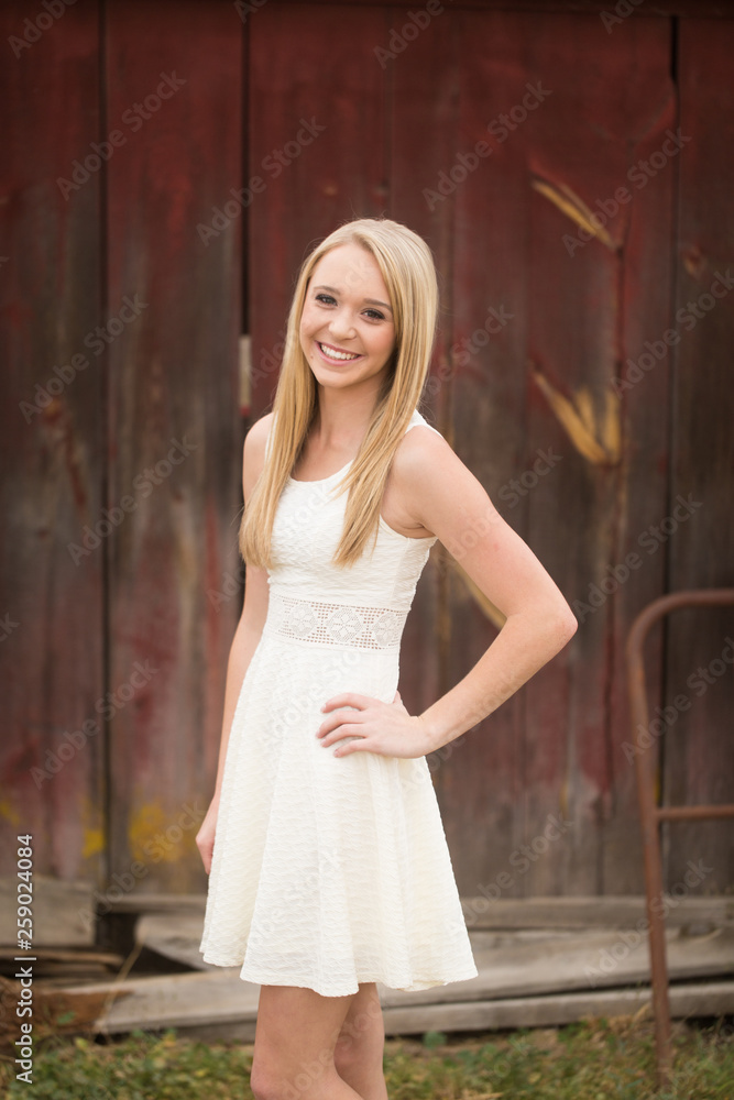 Naklejka premium Beautiful young woman standing in front of old red barn