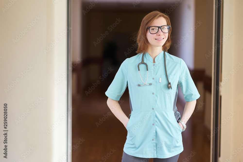 Smiling portrait of white redhead woman doctor with stethoscope on neck and hands in the pockets Smiling portrait of white redhead woman doctor with stethoscope on neck and hands in the pockets