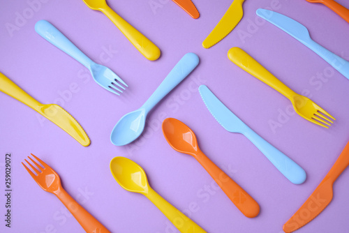 Many colorful plasic forks  spoons and knives on violet background with copy space  top view.