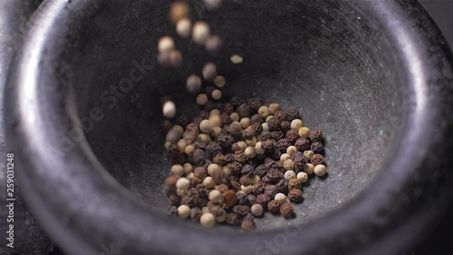 Pour black and white pepper into a mortar. Slow motion