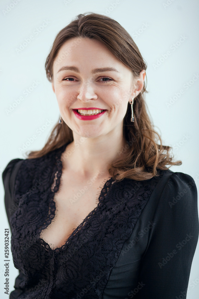 beautiful girl with red lipstick and in a black dress smiles. She is standing against a gray background beautiful girl with red lipstick and in a black dress smiles. She is standing against a gray background