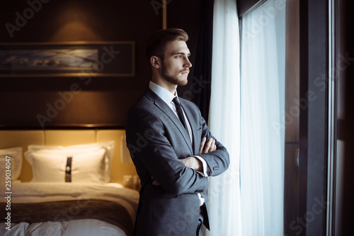 Young handsome man relaxing at his apartment in a hotel after business meeting. Business trip. Booking hotel during your vacation. Businessman in luxury room  of the expensive beautiful hotel.