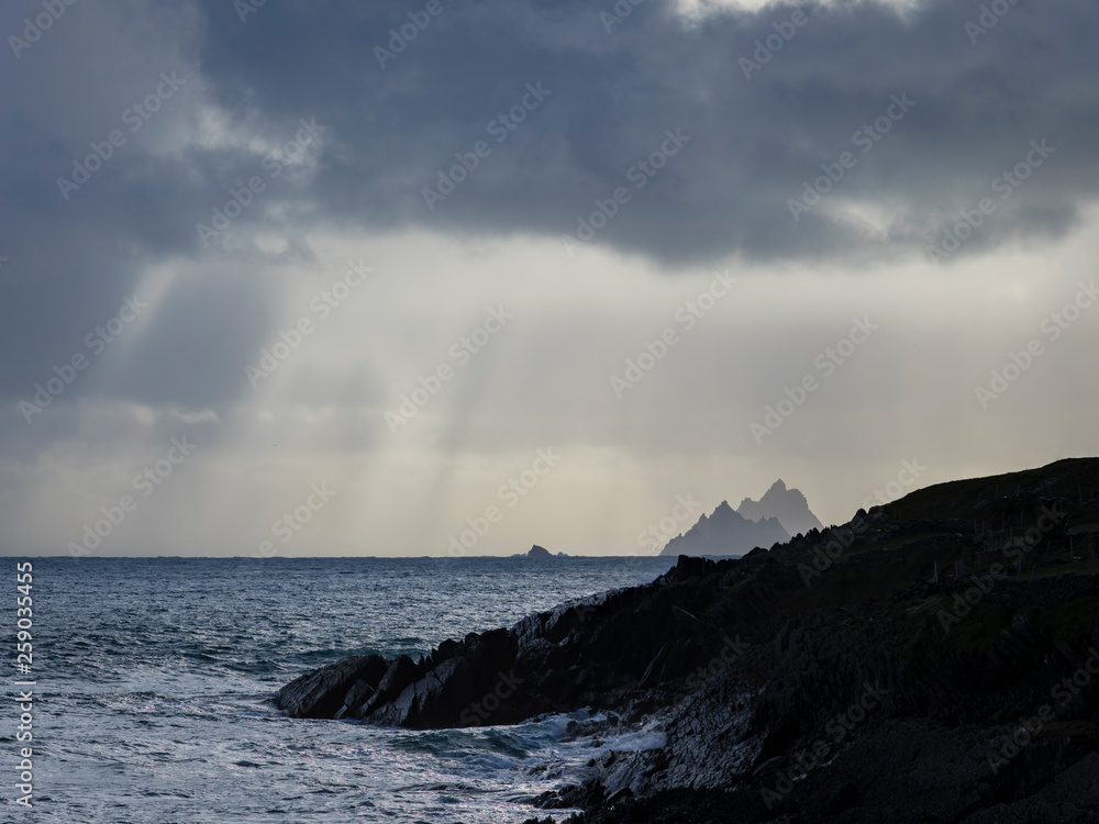 a view of the wild atlantic way off the coast of the ring of kerry in ireland showing skellig michael and surrounding islands in beautiful strong light with cloudy skies 