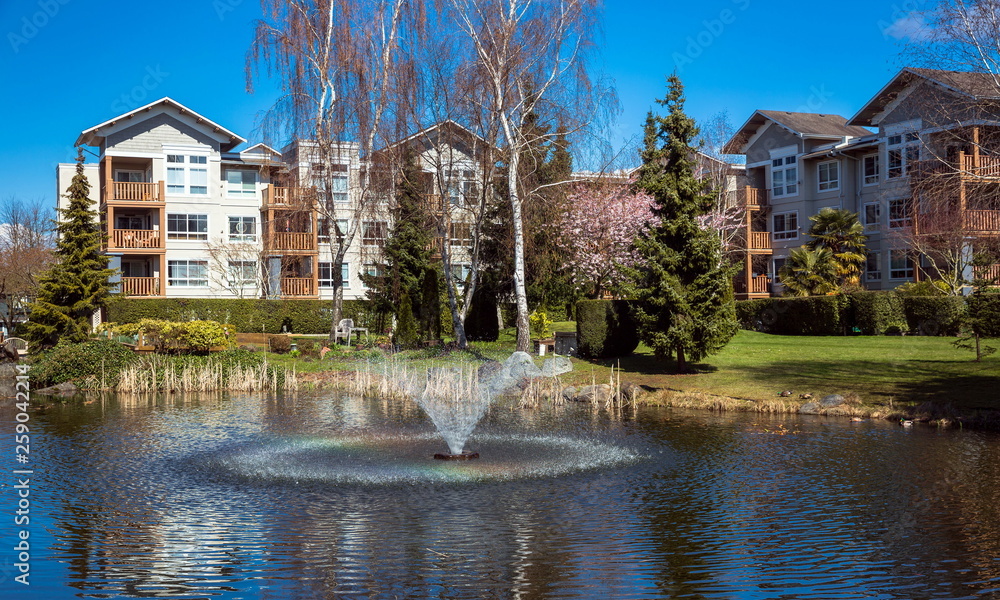 Residential District in Richmond City with pond and fountain, blossom of sakura, green grass bushes and trees in the territory of residential complex, Vanсouver, British Columbia 