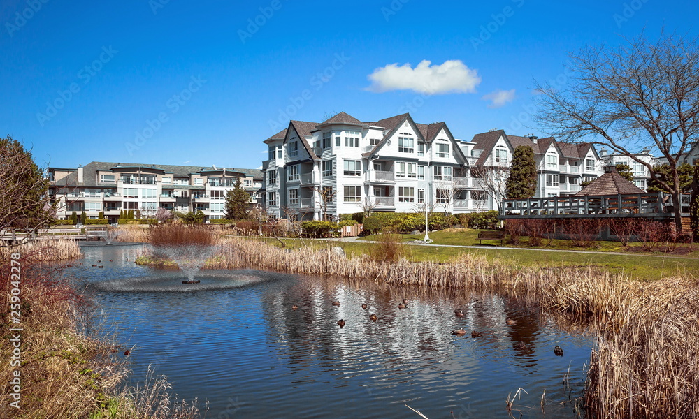 Residential District in Richmond City with pond and fountain, blossom of sakura, green grass bushes and trees in the territory of residential complex, Vanсouver, British Columbia 