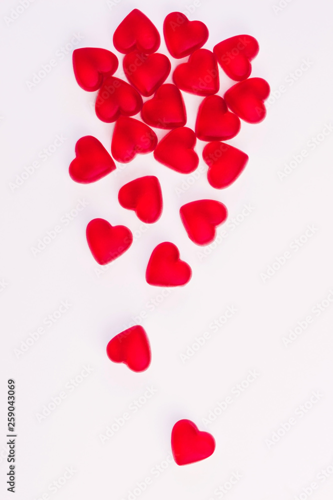 Concept of falling hearts made of heart shaped red jelly sweets on isolated white background. Top view. Copy space.