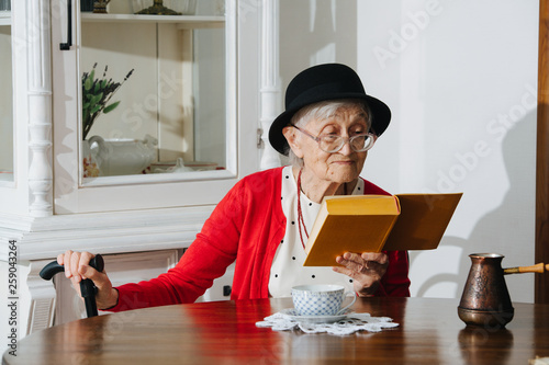 Kind grandmother is reading her book at dinner table at home. photo