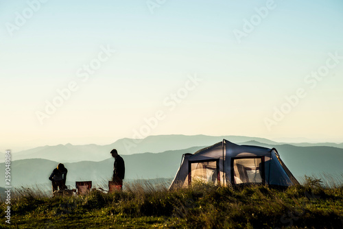 Silhouette of people camping on the top of a mountain at sunset.