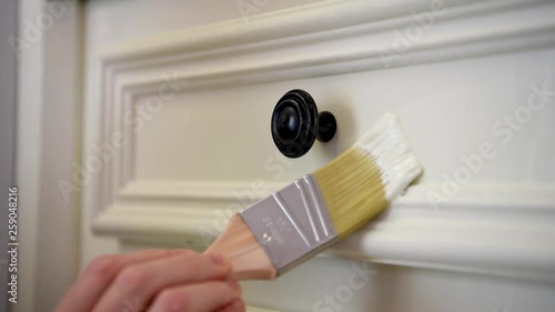 Close-up woman hand painting a white kitchen cabinet, detailed paint job around cabinet knob