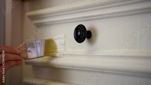 Close-up woman hand painting a white kitchen cabinet, detailed paint job around cabinet knob