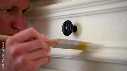 Close-up young blond woman painting a white kitchen cabinet, detailed paint job