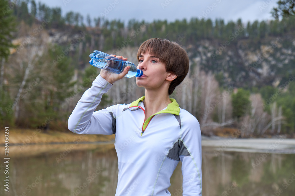 Fitness woman is drinking water from a bottle on a landscape background. Outdoor sports portrait Fitness woman is drinking water from a bottle on a landscape background. Outdoor sports portrait