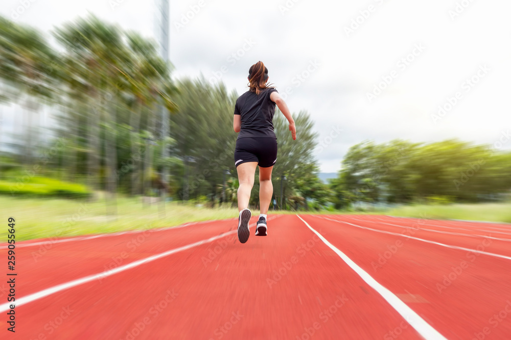 portrait of beautiful young female athlete running on running track (back view) on blur background