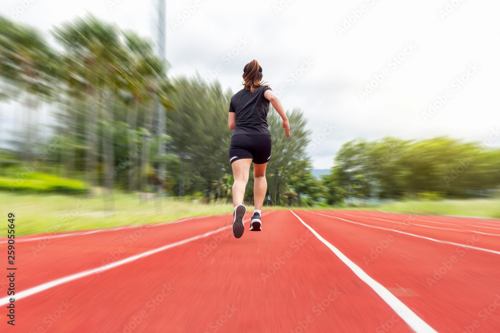 Fototapeta premium portrait of beautiful young female athlete running on running track (back view) on blur background