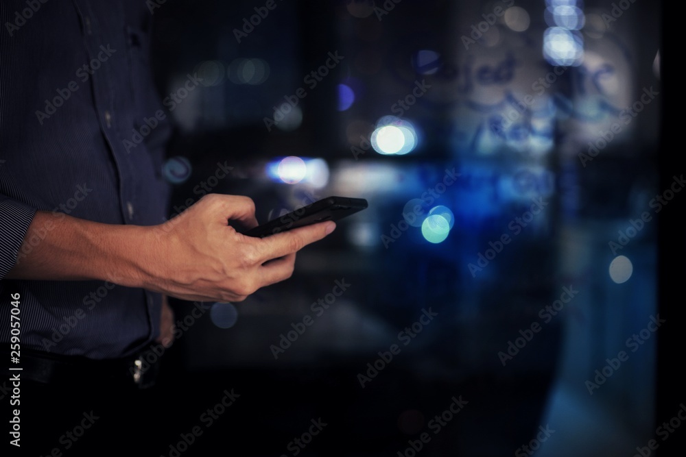 businessman checking on mobile phone in a modern office with out of focus lights in the background. office worker night at the office. modern businessman concepts. businessman checking on mobile phone in a modern office with out of focus lights in the background. office worker night at the office. modern businessman concepts.