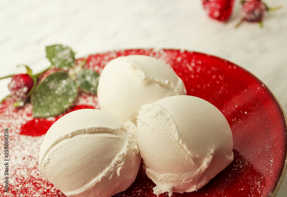 Vanilla ice cream lies on a red plate. Decorated with a red rose. Homemade organic product. Selective focus, side view. Vanilla ice cream lies on a red plate. Decorated with a red rose. Homemade organic product. Selective focus, side view.