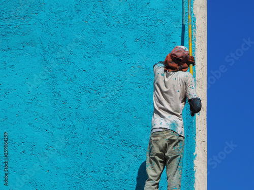 a man paints a wall in blue outdoors. back view