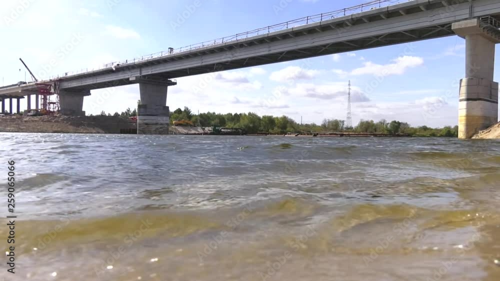 Sunny summer landscape with river, sandy beach and beautiful green trees on the river bank. Construction of a concrete bridge. Construction of an automobile bridge at a construction site. Sunny summer landscape with river, sandy beach and beautiful green trees on the river bank. Construction of a concrete bridge. Construction of an automobile bridge at a construction site.