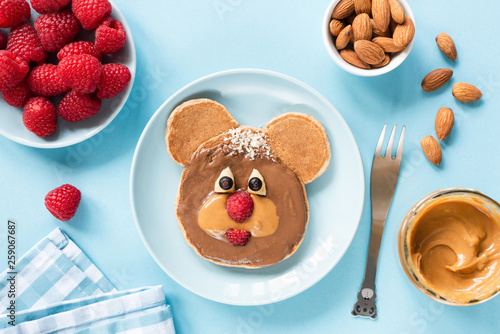 Cute funny pancake food art for kids. Bear or dog shaped pancake with peanut butter and berries. Blue background. Healthy colorful children breakfast