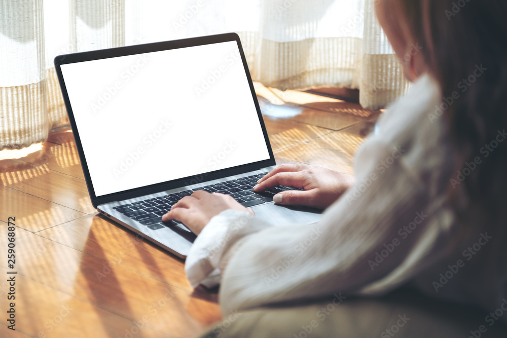 Fototapeta premium Mockup image of a woman typing on laptop computer with blank white desktop screen while laying down on the floor with feeling relaxed