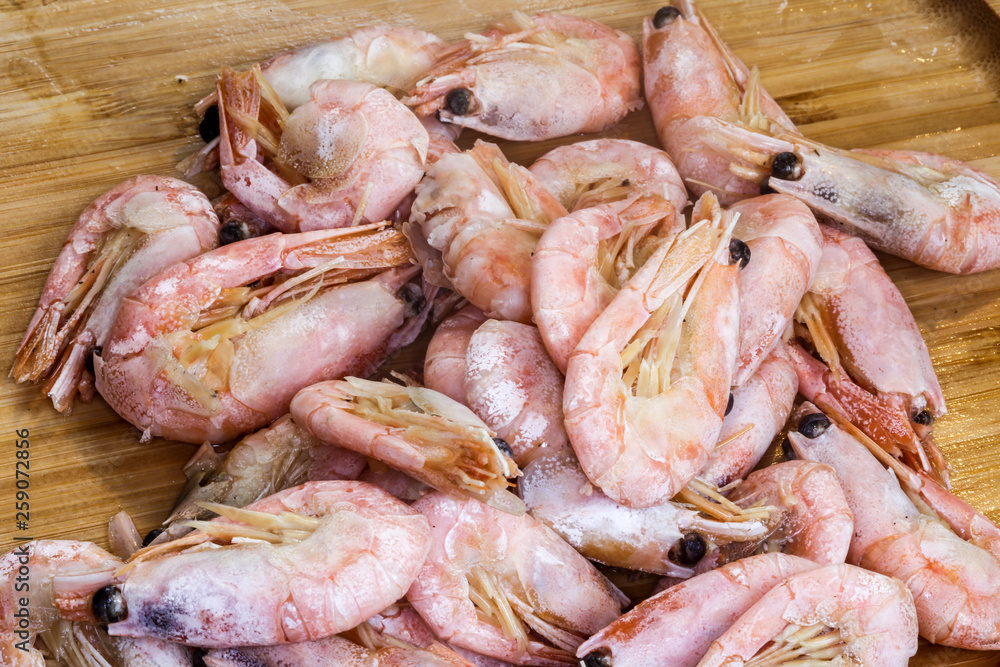 Boiled-freezed shrimps in shells on the wooden cutting board. Boiled-freezed shrimps in shells on the wooden cutting board.