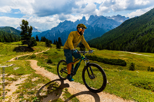 Single mountain bike rider on electric bike, e-mountainbike rides mountain trail. Man cycling on bike in Dolomites mountains. Cycling e-mtb enduro trail track. Outdoor sport activity.