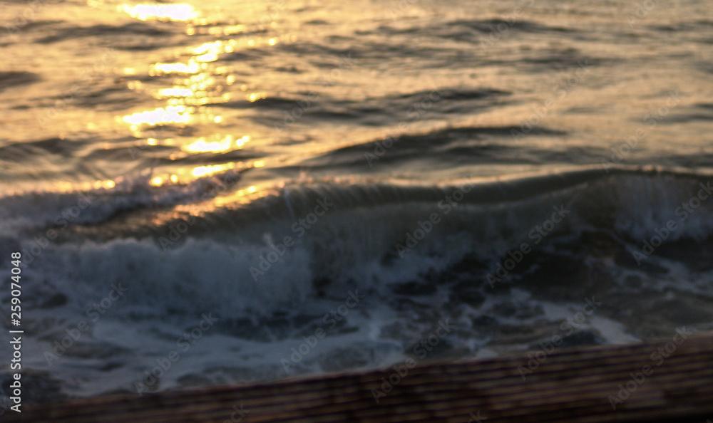 Wave crashing in the sea, at sunset with water drops splashing and flying in the air and warm orange color from the sun