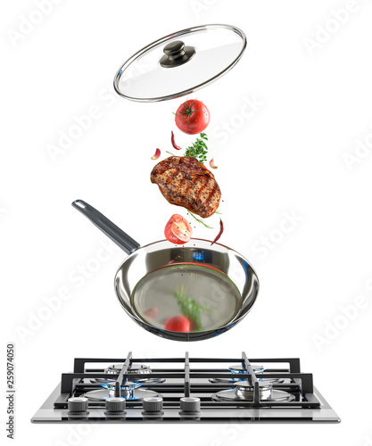 Fresh multicolored vegetables and juicy roasted steak fly over a chrome-plated shiny frying pan and a black glass gas stove on which flames burn. White isolated background