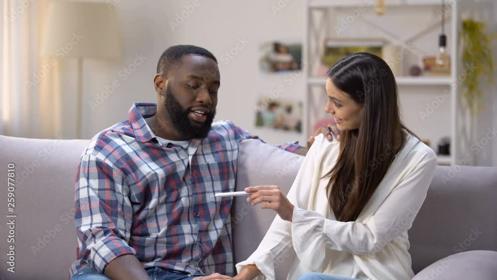 Woman showing pregnancy test to happy Afro-American boyfriend, positive result Woman showing pregnancy test to happy Afro-American boyfriend, positive result