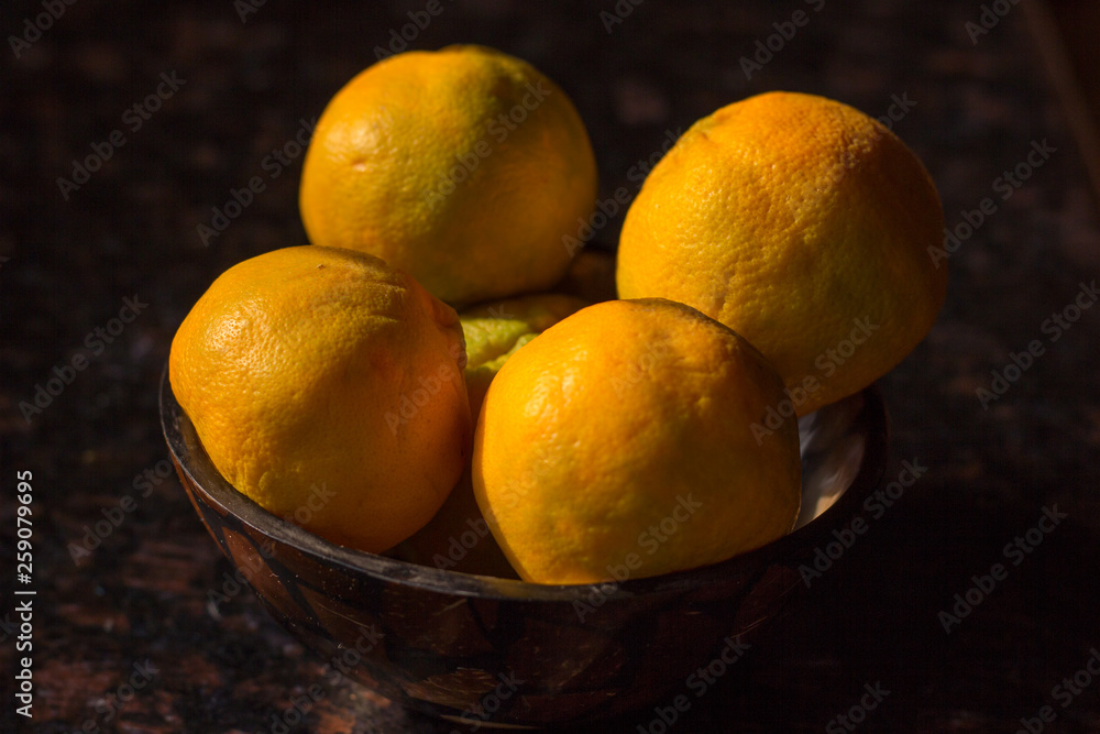 Organic oranges freshly plucked from farm is arranged on a wooden bowl isolated on a black background. Farm fresh oranges organically grown, rich in  vitamin C.