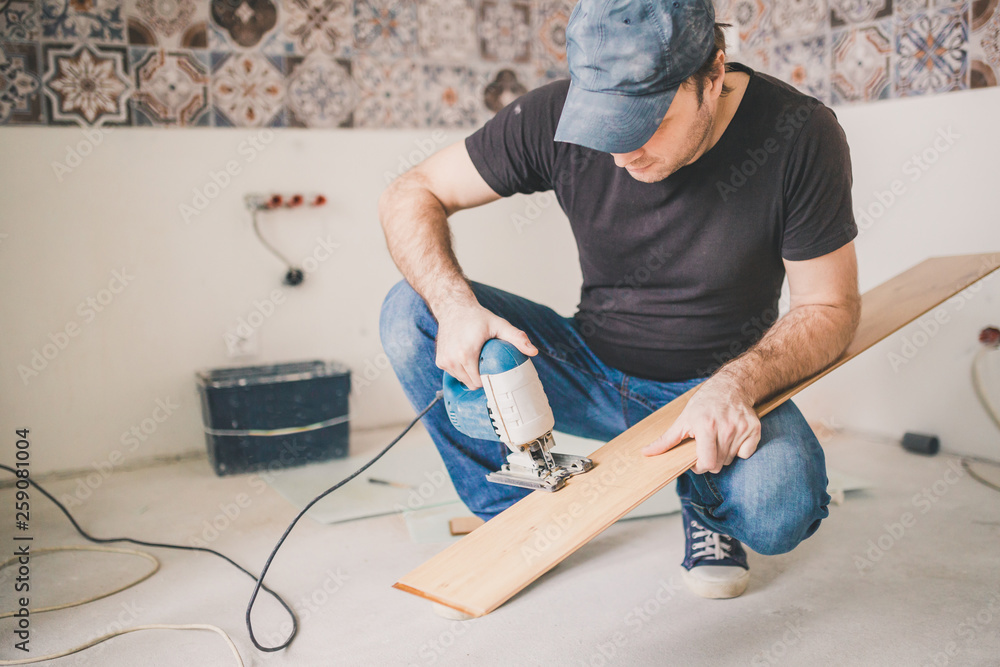 A craftsman cuts a laminate board with an electric jigsaw - flooring A craftsman cuts a laminate board with an electric jigsaw - flooring
