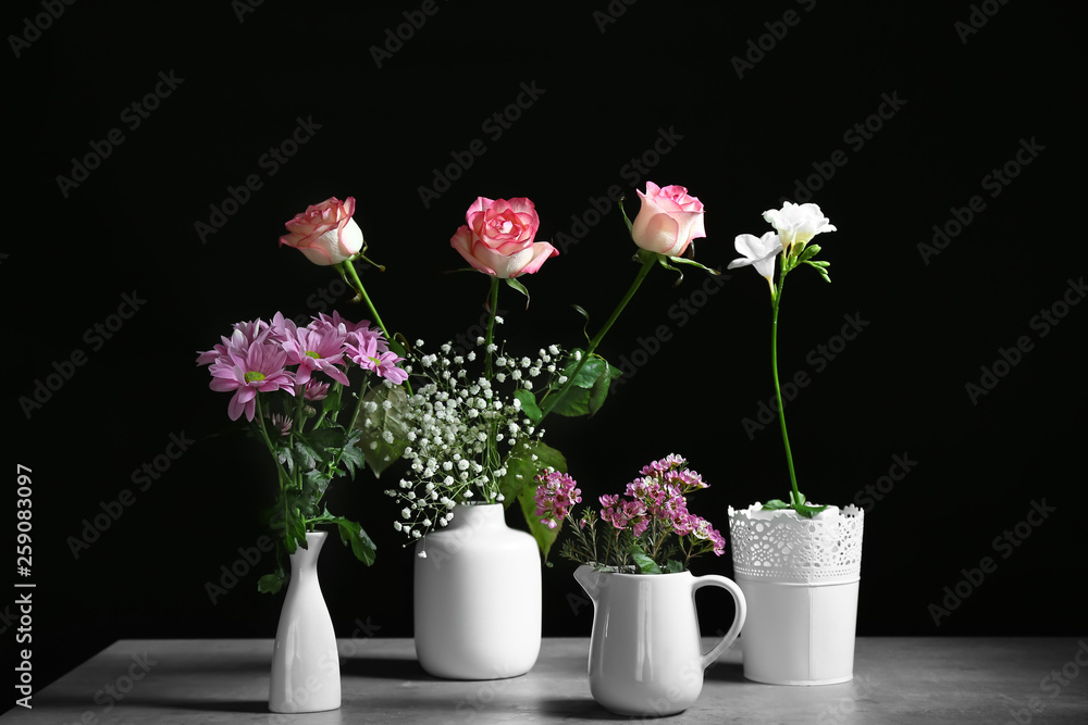 Obraz premium Vases with beautiful flowers on table against dark background
