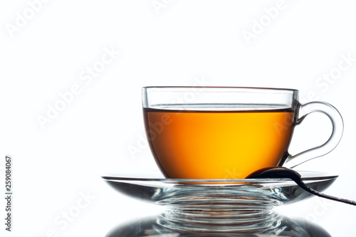 A cup of black tea and a spoon on a white table with reflection