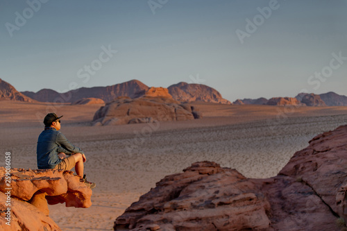 Young Asian man traveler sitting on the rock in Wadi Rum desert looking at sunset, famous place in Jordan. Middle east travel concept