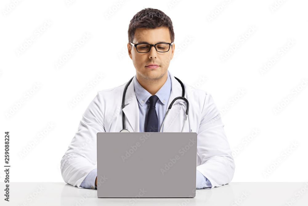 Young male doctor sitting at a desk and working on a laptop Young male doctor sitting at a desk and working on a laptop