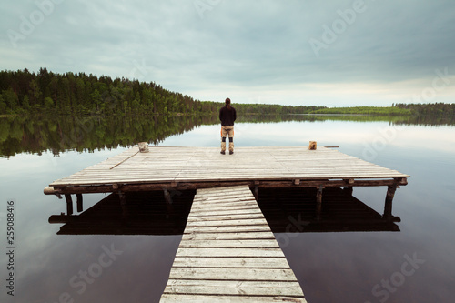 A man stands on a wooden pier on the lake Summer. © Mikhail