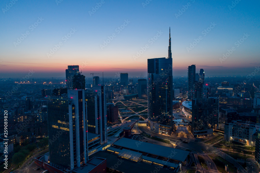 Naklejka premium Mediolan (Włochy) panoramę miasta o świcie, widok z lotu ptaka, przelatujące nad wieżowcami obszaru finansowego w dzielnicy Porta Nuova. Budynek biurowy Unicredit Tower o wschodzie słońca.