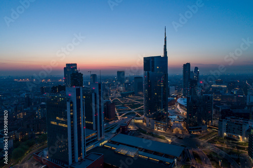 Milan (Italy) city skyline at dawn, aerial view, flying over financial area skyscrapers in Porta Nuova district. Unicredit Tower office building at sunrise.