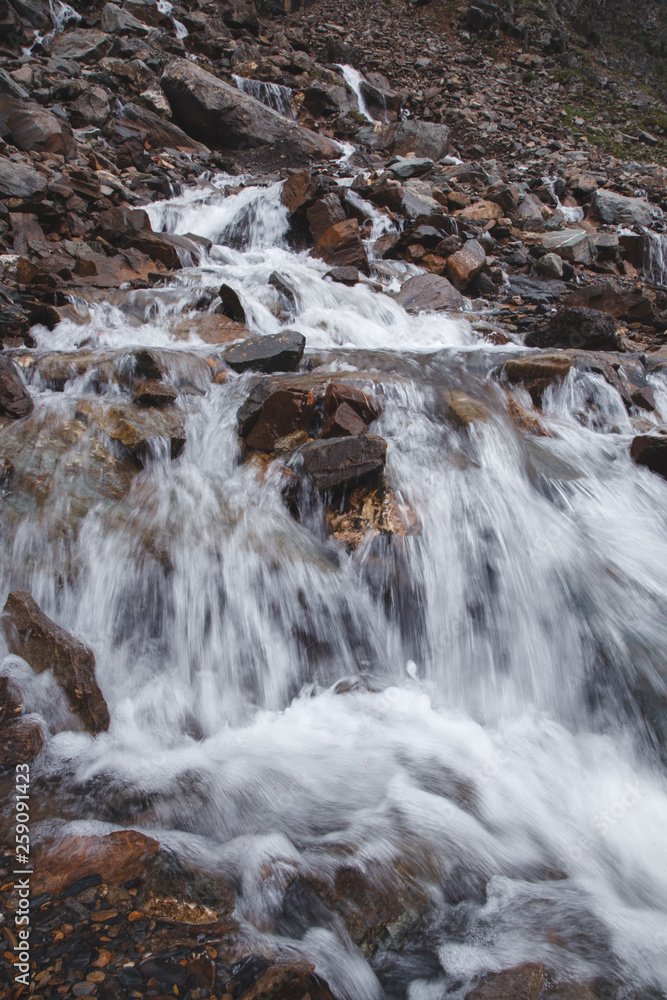 Waterfall in a high gorge among the brown rocks and fog of the Altai mountains. Waterfall in a high gorge among the brown rocks and fog of the Altai mountains.
